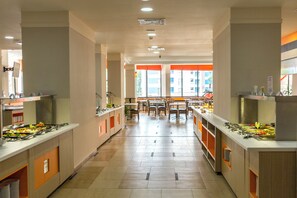 A modern hotel kitchen with buffet counters, dining tables, and chairs.