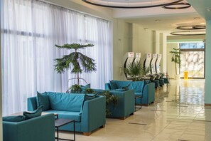 A hotel lobby with teal sofas, large windows with sheer curtains, and potted plants. - Kuban Resort and Aquapark (Nessebar)