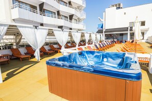 Cubierta de crucero con varias tumbonas, una bañera de hidromasaje y un bar.
