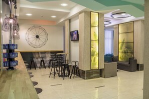 A modern bar area with a wooden counter, black stools, a geometric wall decoration, and a television screen.