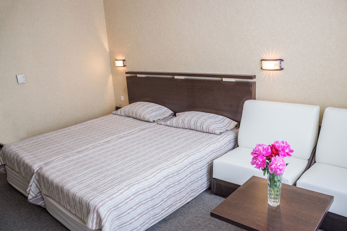 Une chambre d’hôtel avec un lit, un canapé blanc, une petite table et un vase rempli de fleurs.