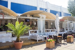 An outdoor seating area with white furniture, a large potted plant, and a sign for a sushi restaurant. - Kuban Resort and Aquapark (Nessebar)