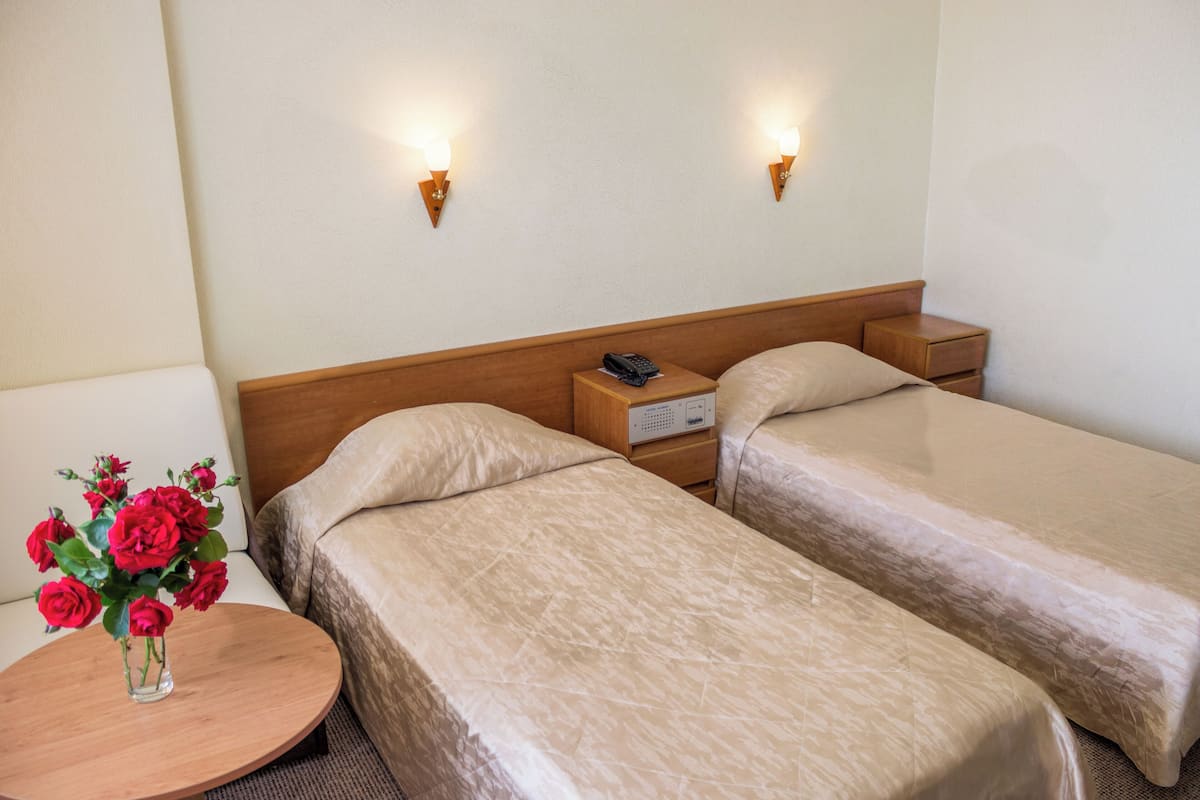 Een hotelkamer met twee bedden, een nachtkastje met een bloevas en twee wandlampen.