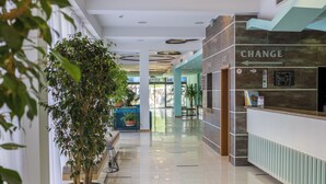 Un hall d’entrée moderne avec un comptoir d’accueil, un grand arbre en pot et un panneau indiquant un changement.