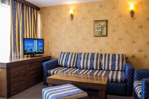 Una habitación con sofá, reposapiés, mesa de madera y un televisor mostrando una pantalla.