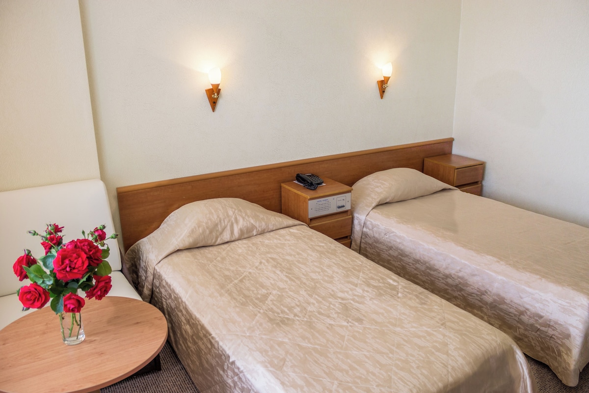 Une chambre d’hôtel avec deux lits, une table de chevet ornée d’un vase de fleurs et deux lampes fixées au mur.