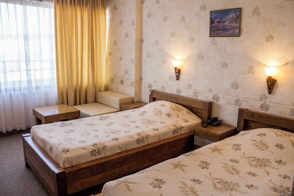 Een hotelkamer met twee bedden, een nachtkastje met telefoon, een klein zitgedeelte en een wandlamp.