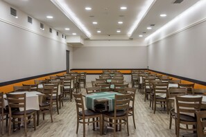 Un salón de conferencias con varias mesas y sillas, luces empotradas en el techo y una pared de acento en tonos negros y naranjas.