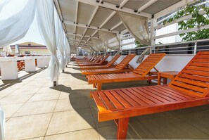 Un espace extérieur aménagé, abrité et doté de chaises longues en bois et de rideaux blancs.
