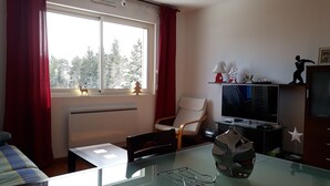 Una sala de estar con una mesa de vidrio, una silla, un televisor y una ventana con cortinas.