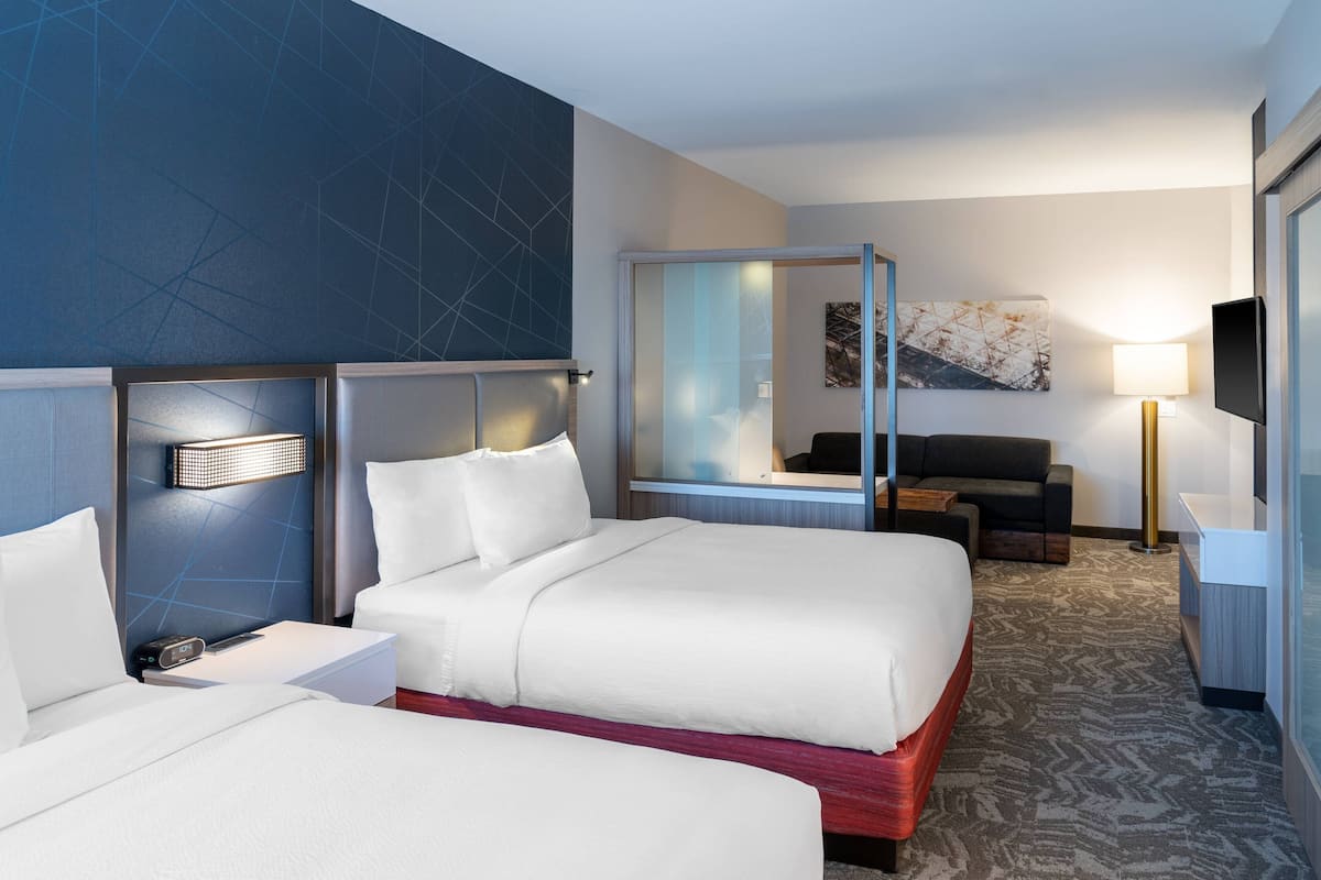 A hotel room with two beds, a sofa, a desk, a TV, and a large mirror.
