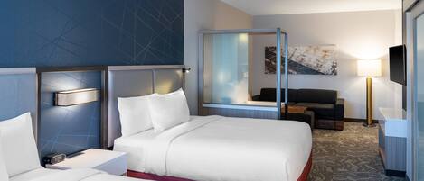 A hotel room with two beds, a sofa, a desk, a TV, and a large mirror.