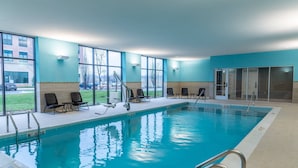 An indoor swimming pool with clear glass walls, a tiled floor, and a few lounge chairs.