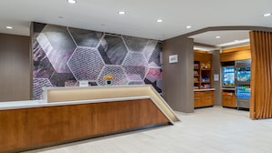 A modern reception area with a wooden counter, a hexagonal patterned wall, and a vending machine.
