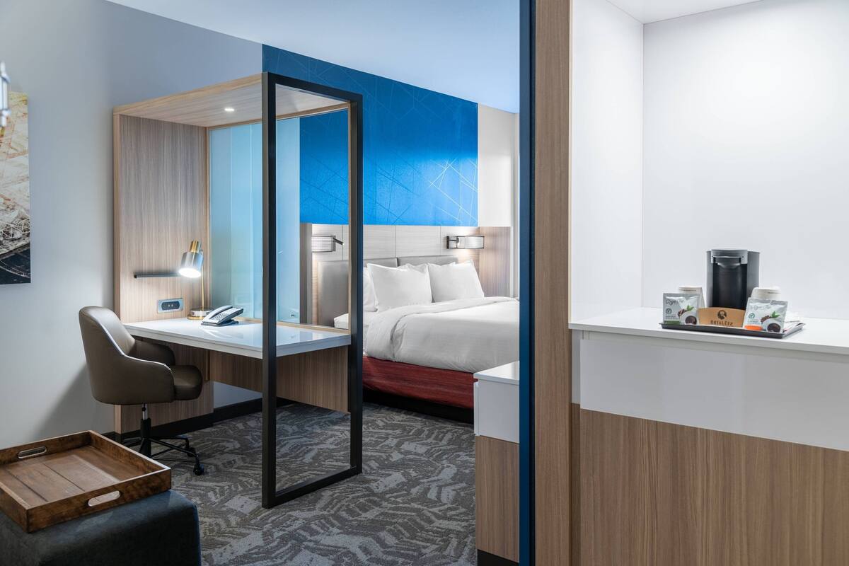 A hotel room with a desk, chair, bed, and a coffee station.