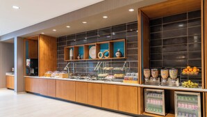 A buffet area with a variety of food items, including fruits and beverages, and a wooden counter.