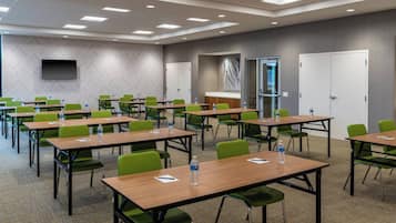 A conference room with multiple tables and chairs, equipped with water bottles, and a flat-screen TV mounted on the wall.