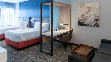 Une chambre d’hôtel avec deux lits, un bureau, une chaise, une table d’appoint en bois et un tableau au mur.