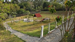 A playground with swings and a small red-roofed structure, surrounded by a stone pathway and greenery. - Sítio Santa Filomena São Roque/SP (São Roque)
