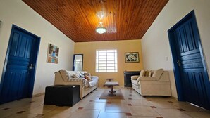 A living room with two sofas, a coffee table, and a fireplace. There are two blue doors and a window with blinds. - Sítio Santa Filomena São Roque/SP (São Roque)