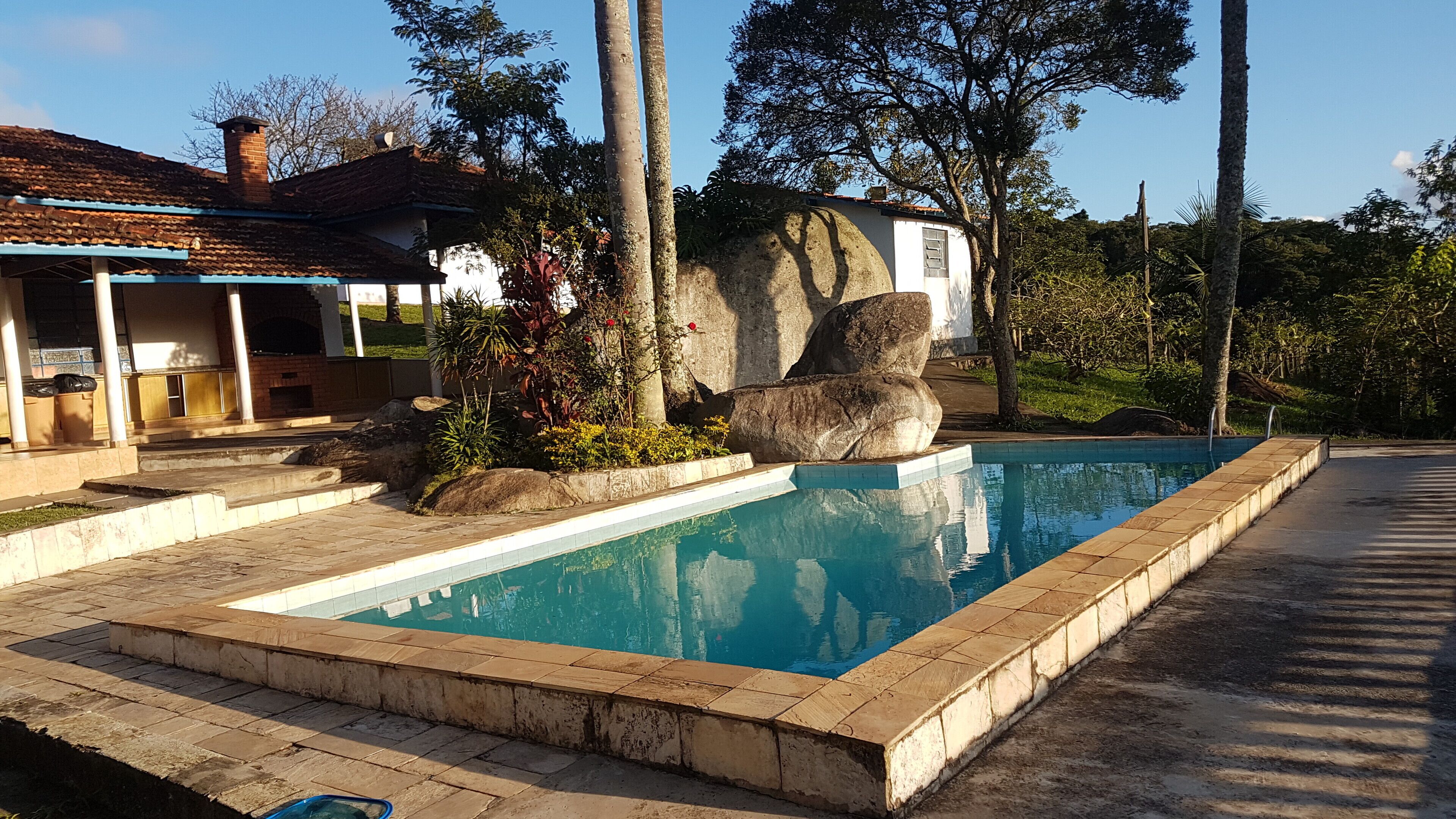 A swimming pool with a stone border, a covered patio area, and a stone structure with a chimney.
