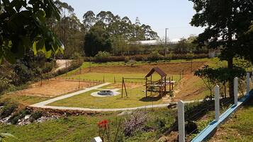 A playground with a swing set and a small shelter, surrounded by a fenced area and greenery.