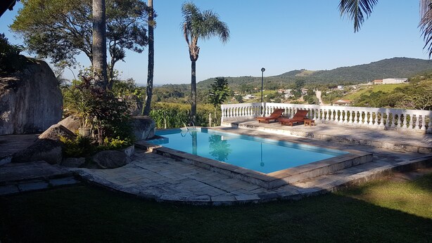 A swimming pool with a stone deck, surrounded by greenery and a white fence. - Sítio Santa Filomena São Roque/SP (São Roque)