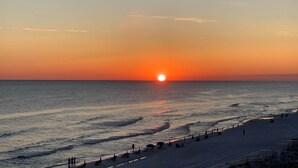 A beach with the sun setting over the horizon, waves gently lapping at the shore, and people walking along the beach.