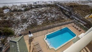 A rooftop pool with a view of the beach, surrounded by a fence and a wooden deck.