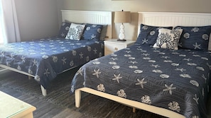 Two twin beds with matching headboards and footboards, a bedside table with a lamp, and a small table in the foreground. - Blue Dolphin 403 Penthouse (Fort Walton Beach)