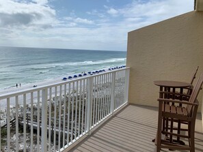 A balcony with a view of the beach, a wooden chair, and a table. - Blue Dolphin 403 Penthouse (Fort Walton Beach)