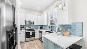 A modern kitchen with white cabinets, stainless steel appliances, a blue tiled backsplash, and a white island with stools. - Sandy Toes Gated Community*Pool*Gym*Beach Svc! (Miramar Beach)