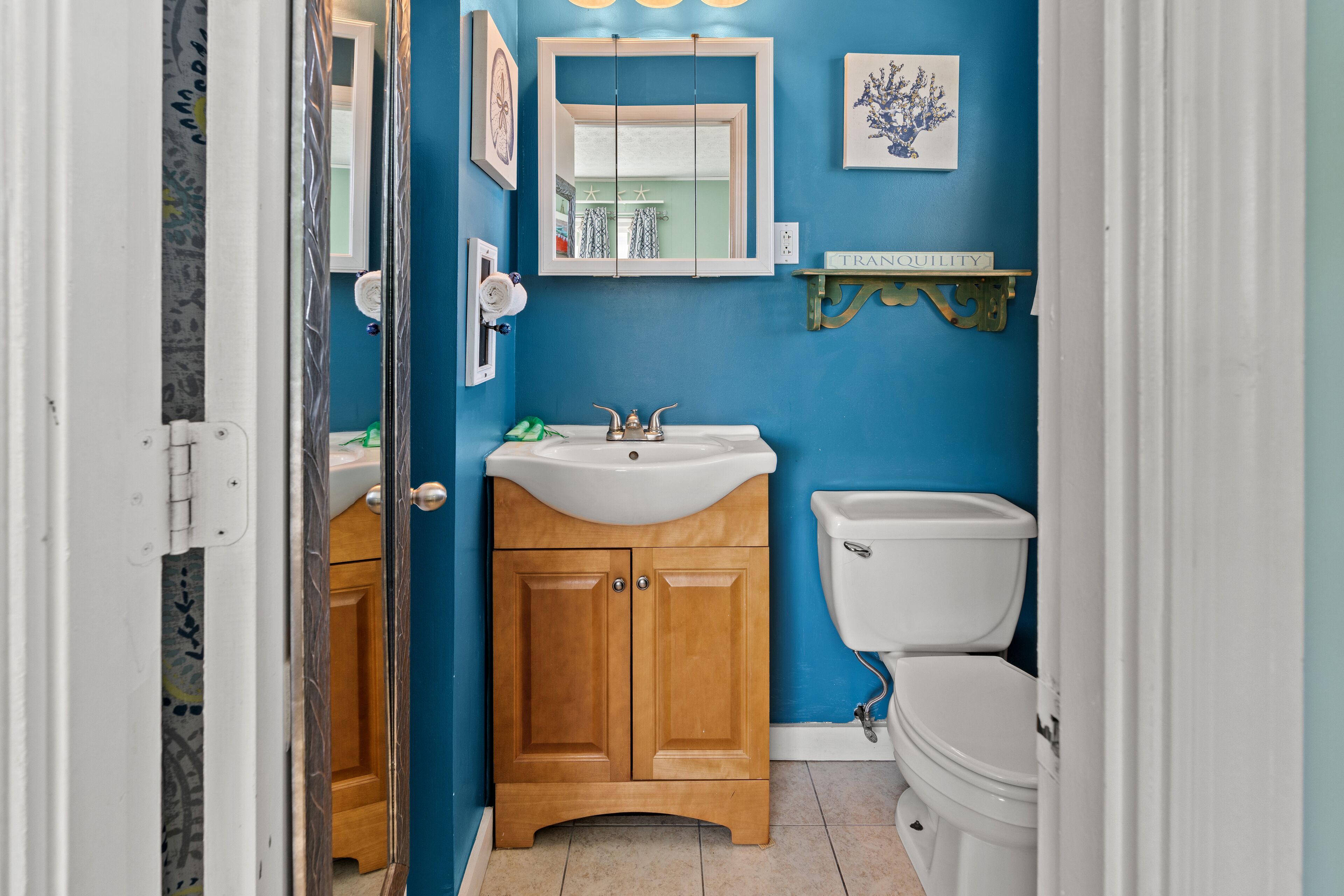 A bathroom with a blue wall, wooden cabinets, a white sink, and a toilet.
