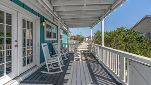 Une véranda couverte avec des balustrades blanches, des fauteuils à bascule et une porte à panneaux de verre.