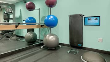 A gym with exercise equipment, including a mirror, a wall-mounted TV, and a standing bike.