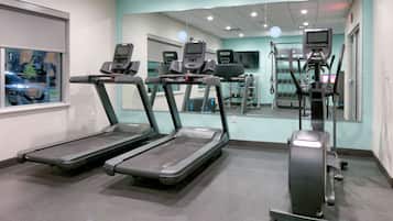 Un gimnasio con cintas de correr, máquinas de pesas y un espejo grande.