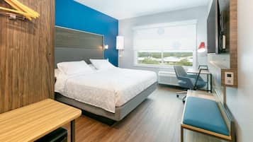 A modern hotel room with a bed, desk, chair, and a large window offering a city view.