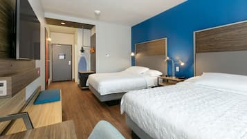Habitación de hotel con dos camas, un escritorio, una silla, un televisor y un baño visible a través de una puerta abierta.