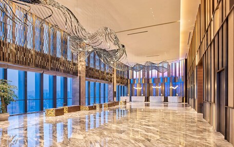 A spacious lobby with a reflective marble floor, large windows offering city views, and a modern ceiling design.