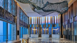 Un hall d’entrée spacieux au design moderne, avec un grand comptoir d’accueil, un sol en marbre et une sculpture au plafond qui le rend unique.