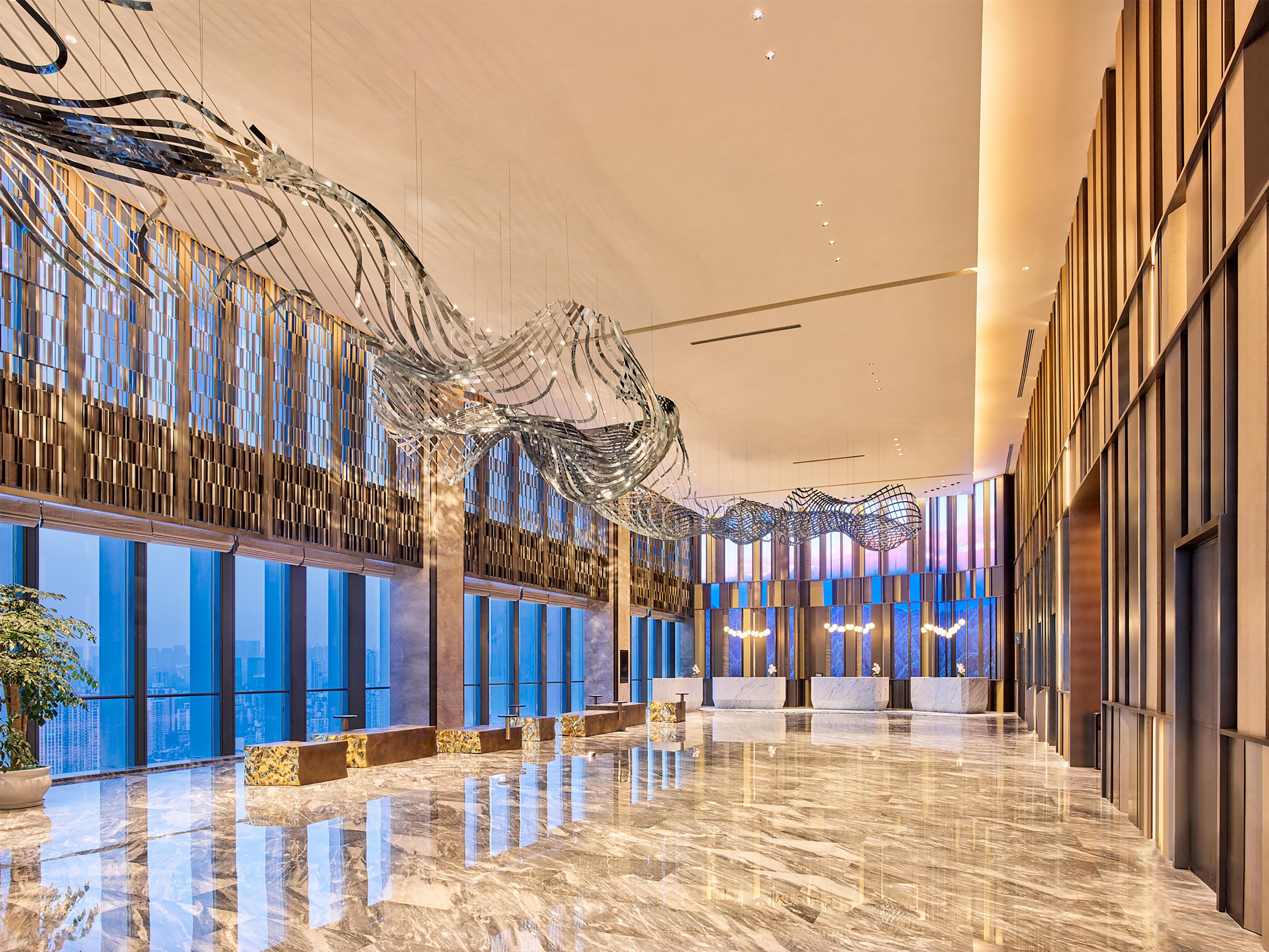 A spacious lobby with a reflective marble floor, modern lighting fixtures, and a large, abstract metal sculpture.