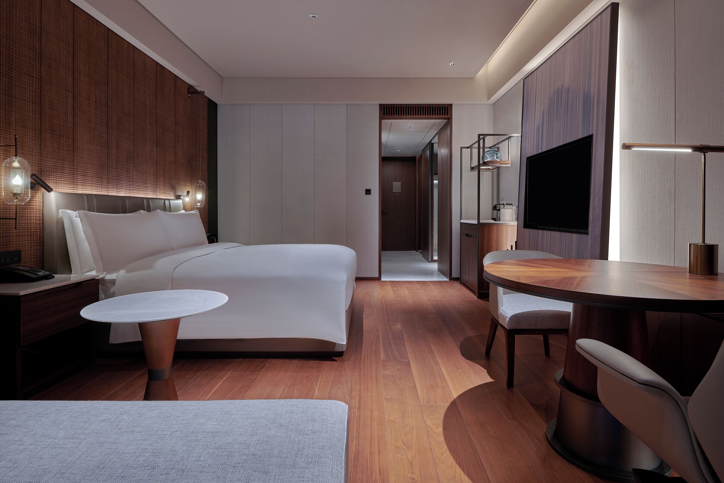 A modern hotel room with a large bed, a dining table, and a TV.