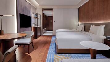 A modern hotel room with a large bed, a desk, a chair, a TV, and a small table.