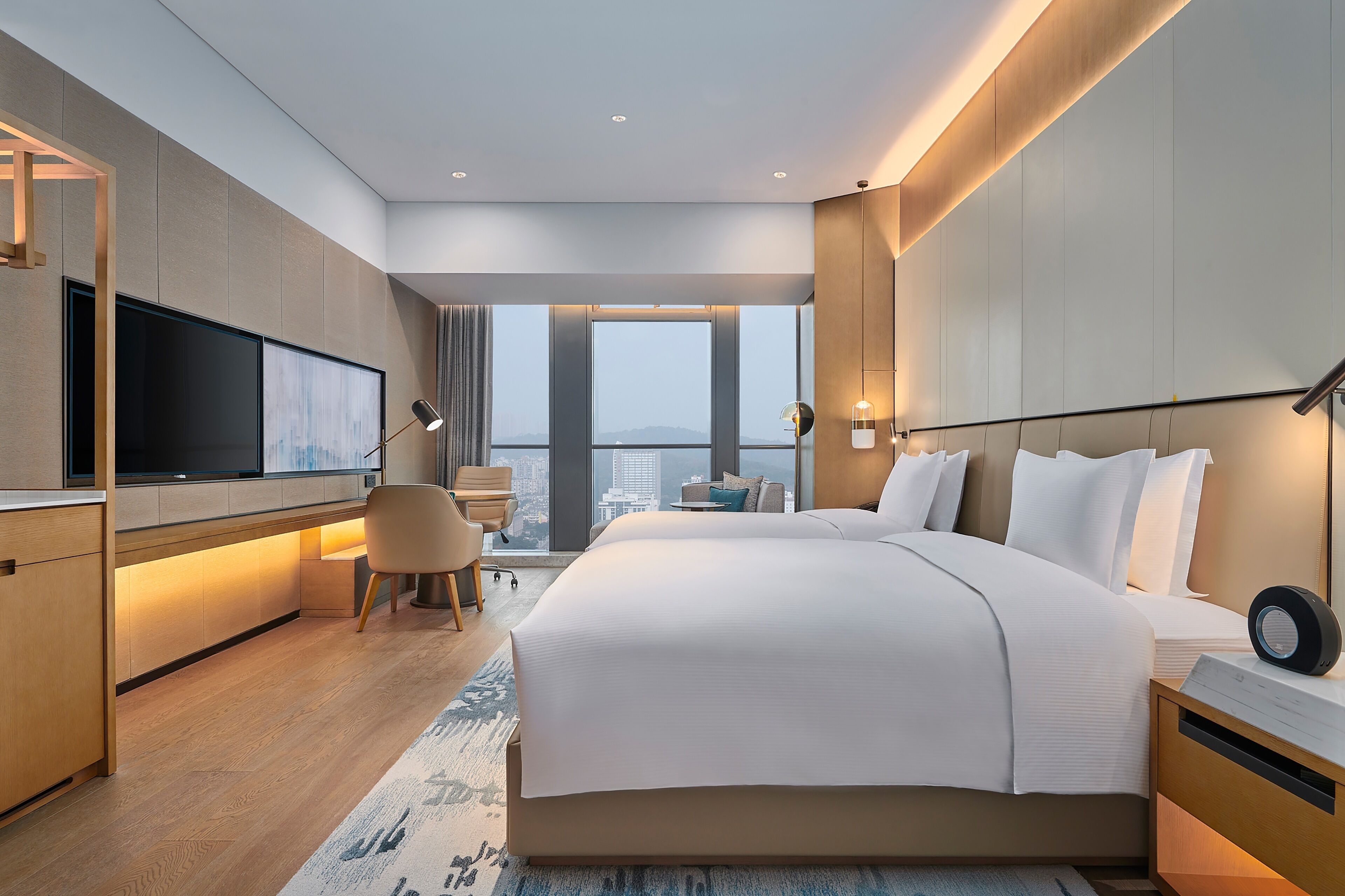 Habitación de hotel moderna con una cama grande, un escritorio, un televisor de pantalla plana y vistas a la ciudad.