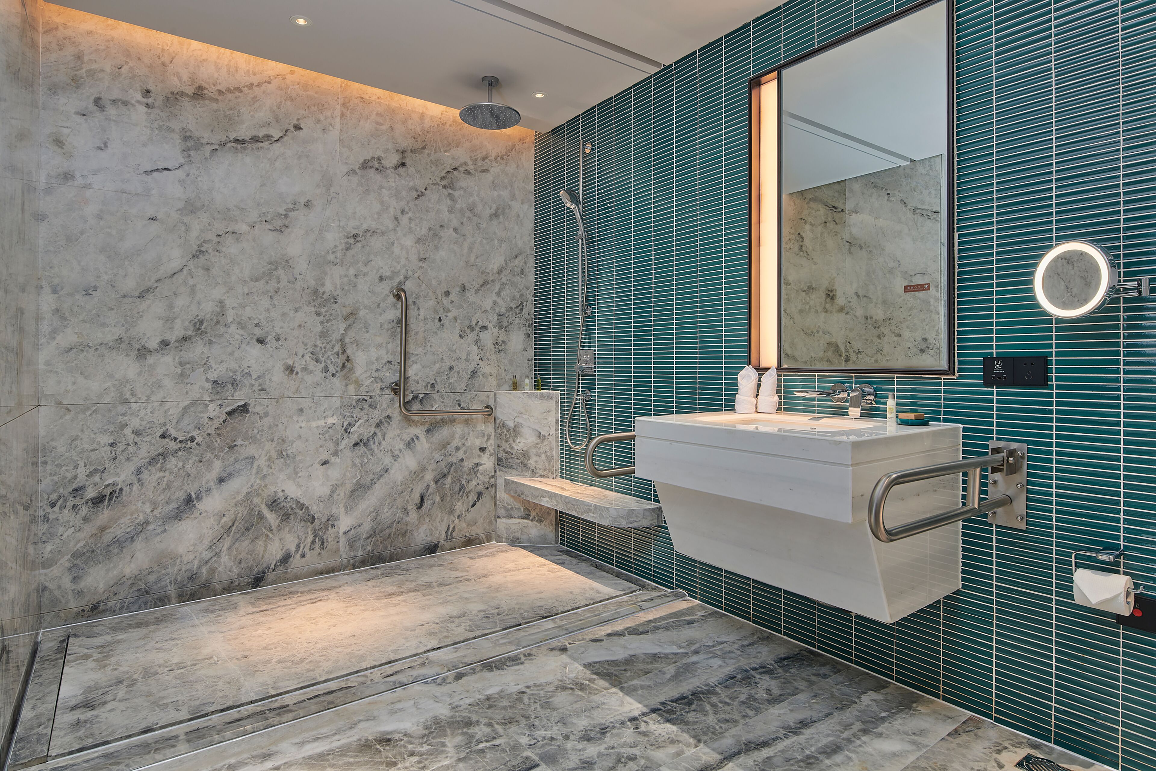Un baño moderno con ducha de mármol, lavamanos con espejo y paredes con azulejos verde mar.