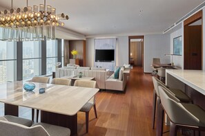 A modern hotel room with a dining area, a living room with sofas, a TV, and a city view.