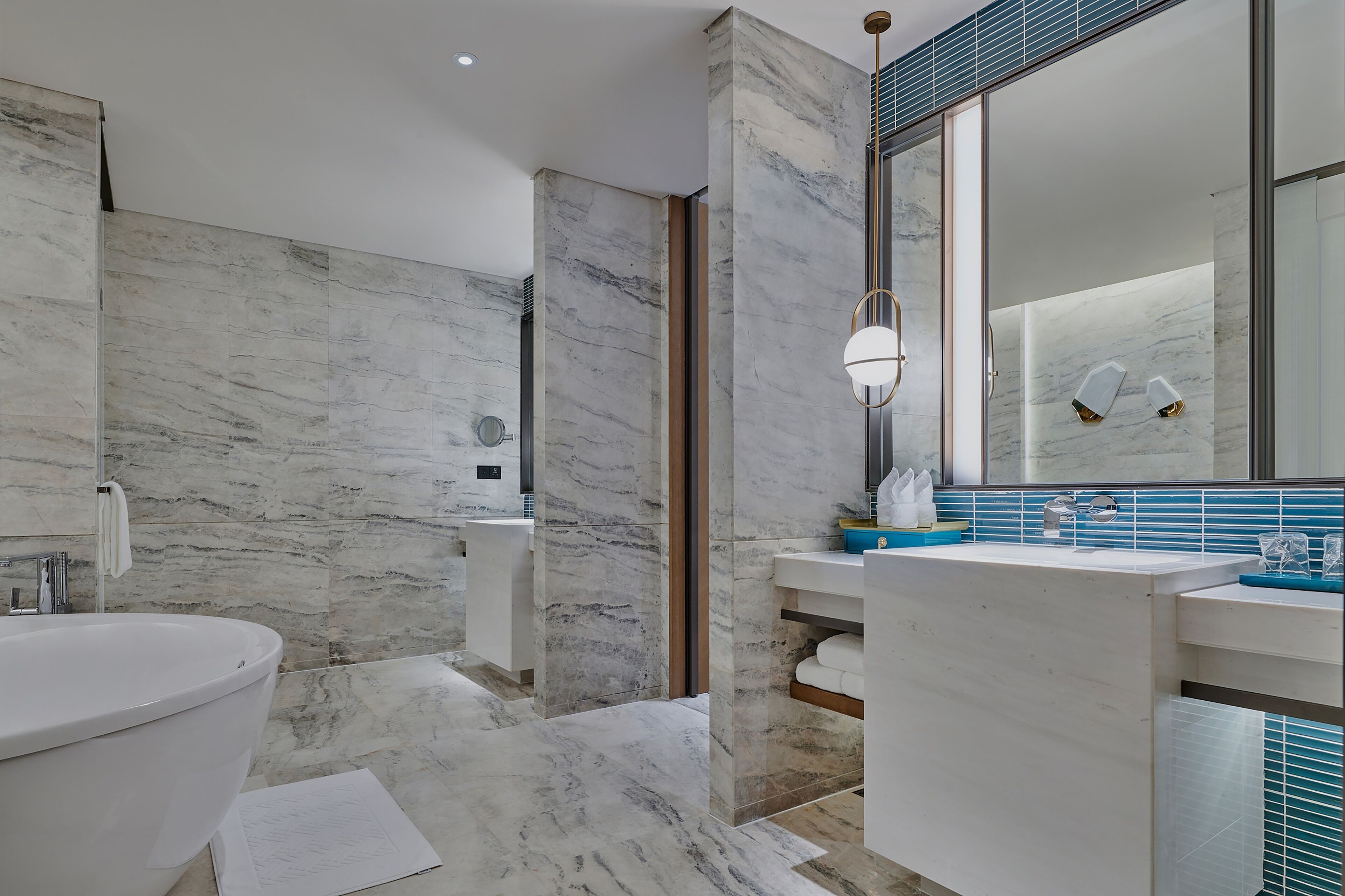 Un baño moderno con un lavabo grande de mármol, una bañera y un espejo con detalles de azulejos azules.
