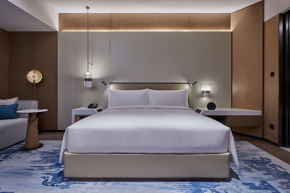 Une chambre d’hôtel moderne, dotée d’un grand lit, de tables de chevet, d’un bureau et d’un canapé.