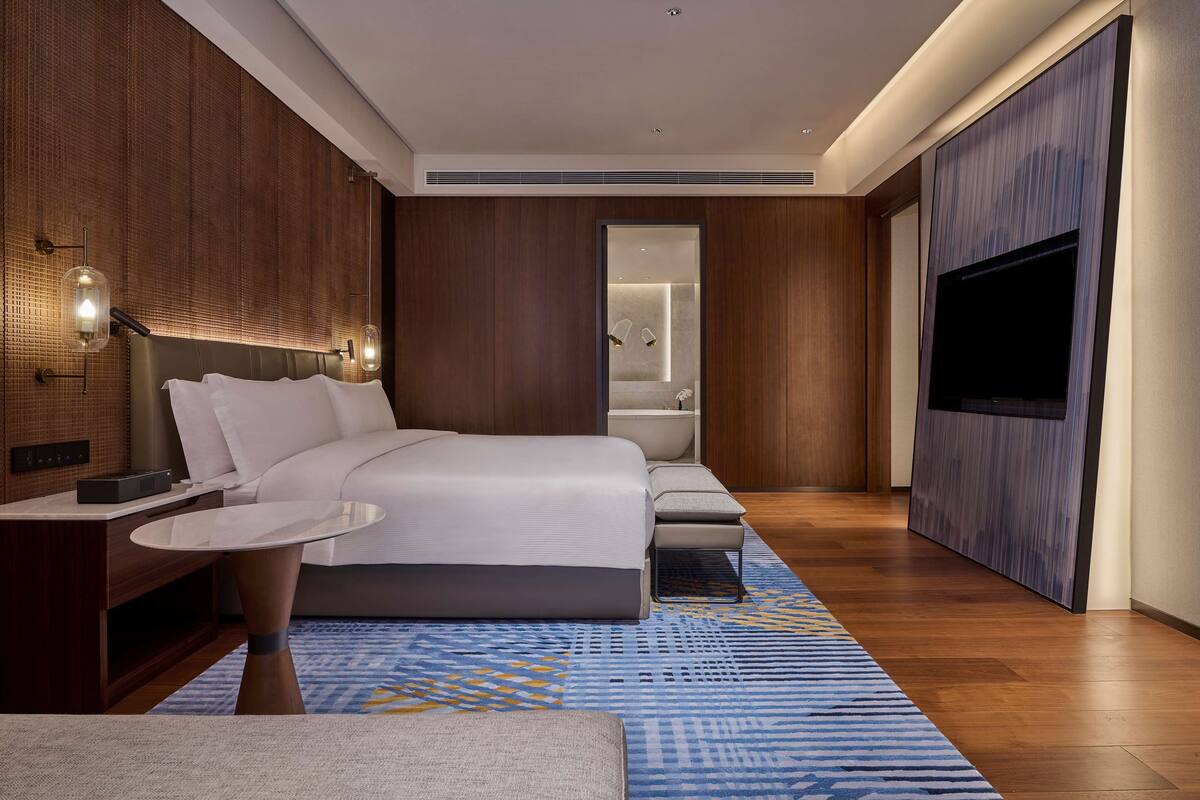 Une chambre d’hôtel moderne avec un grand lit, une table de chevet et un téléviseur à écran plat.
