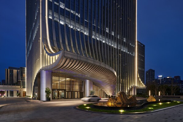 A modern building with a curved entrance and a landscaped area with a reflective water feature.